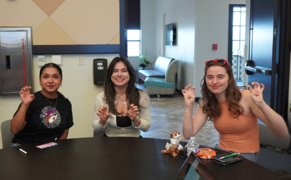 Three students posed together at a table doing a "Paws Up" motion.