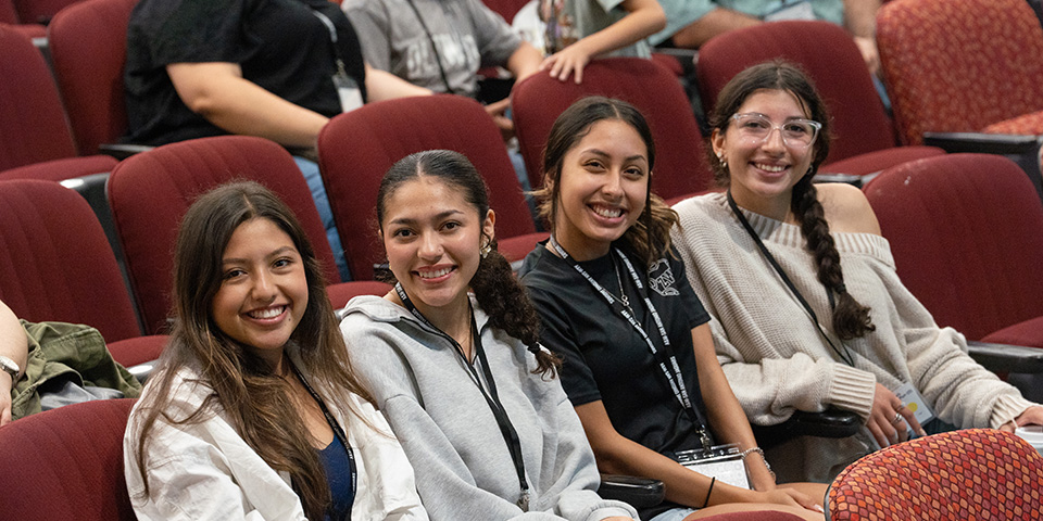 4 girls sitting down in auditorium smiling. 